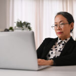 Smiling senior businesswoman wearing elegant formal suit using l